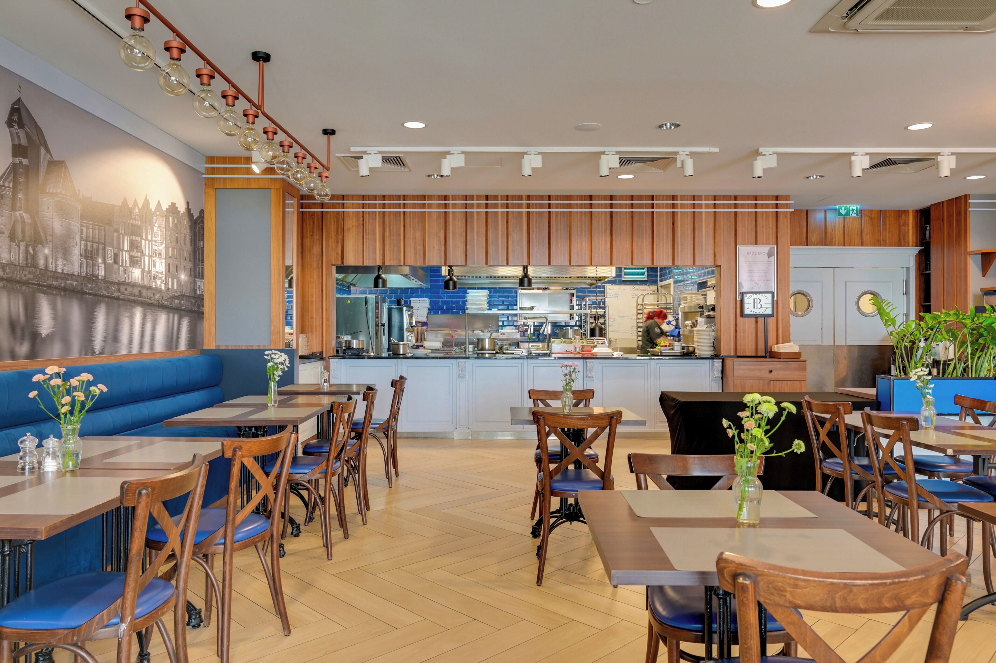 A restaurant with wooden paneling, blue cushioned seating, and a view of the kitchen.