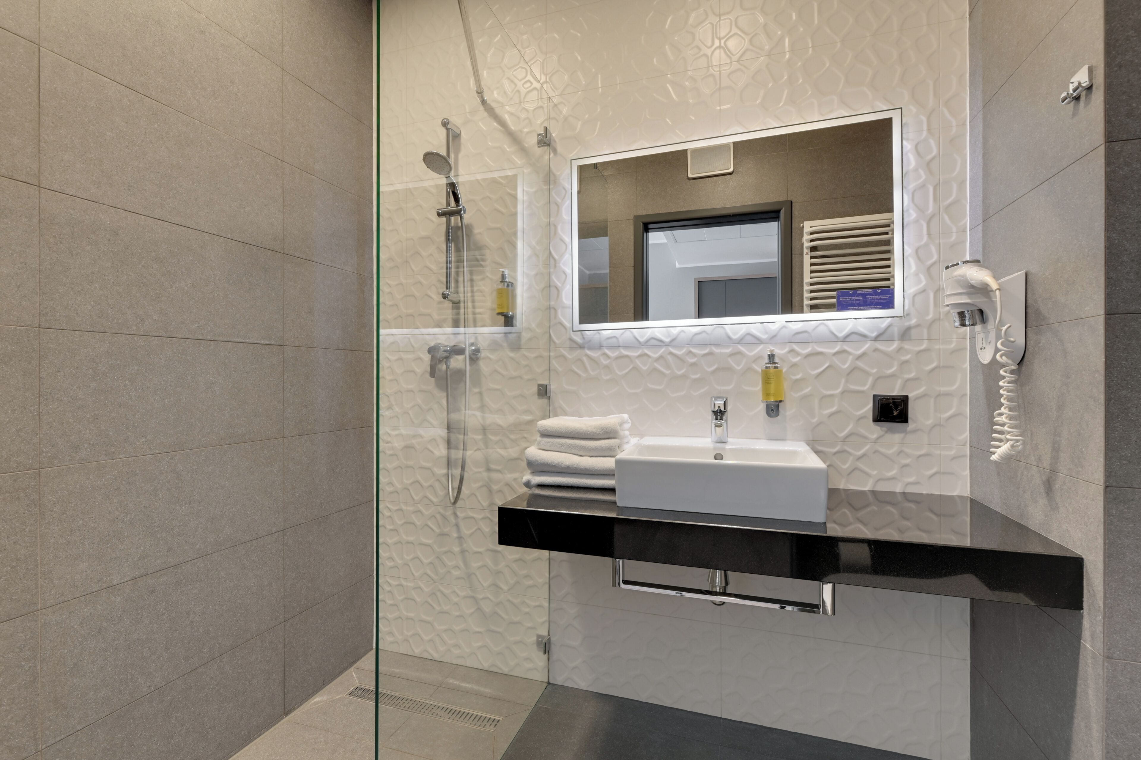 Un bagno moderno con cabina doccia in vetro, un lavandino bianco con piano di appoggio nero e uno specchio a parete.
