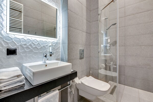 Un baño moderno con un lavamanos blanco, un inodoro y una ducha con mampara de vidrio.