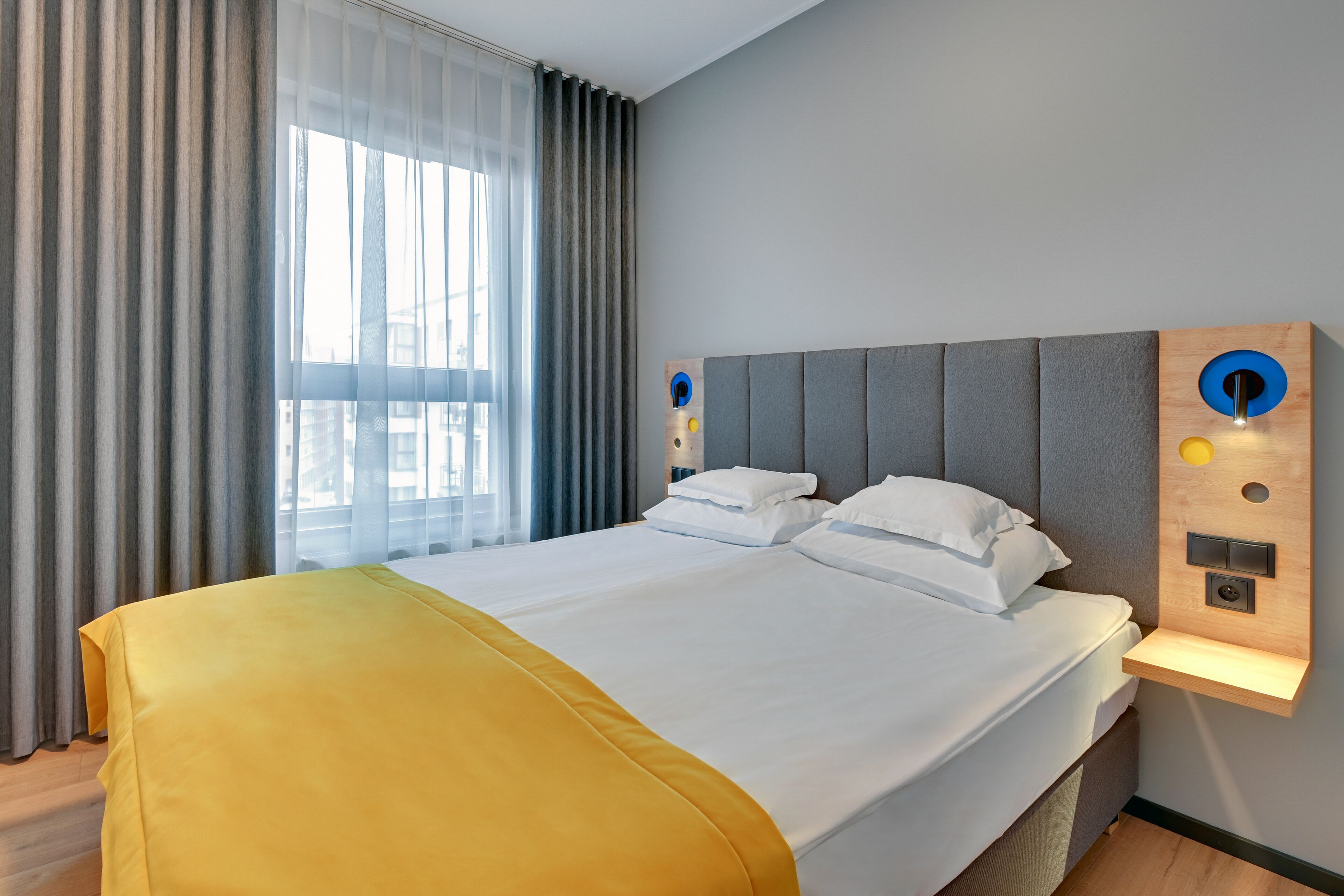 A hotel room with a large bed, a bedside table with a built-in lamp, and a window with curtains.