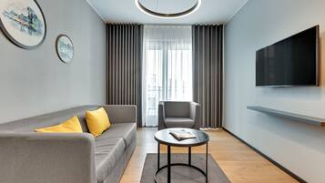 Una sala de estar moderna con un sofá gris, una mesa de centro redonda, un sillón gris y un televisor de pantalla plana montado en la pared.