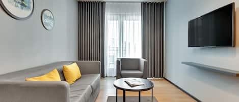 Un salon moderne avec un canapé gris, une table basse ronde, un fauteuil gris et un téléviseur à écran plat fixé au mur.