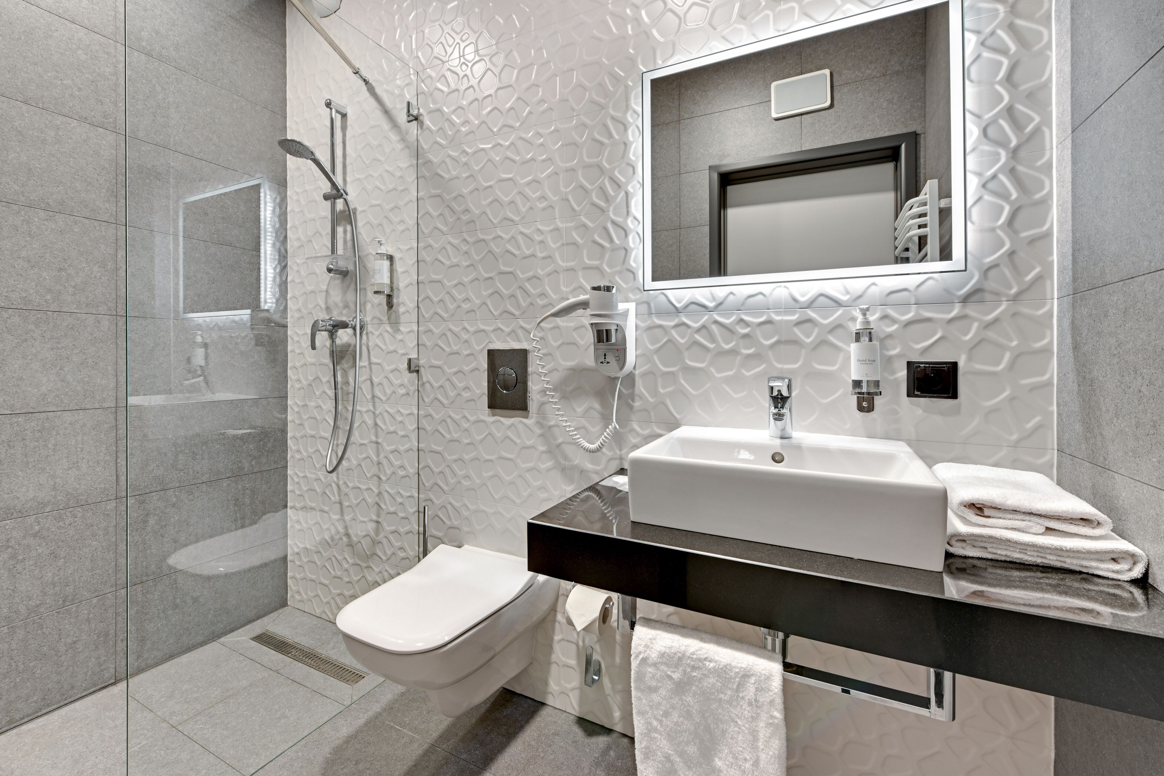 A modern bathroom with a glass shower enclosure, a white toilet, a black countertop with a sink, and a mirror above the sink.
