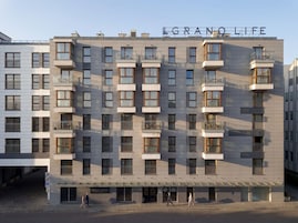 Um hotel com vários andares e varandas, com uma placa visível que diz 'GRANOLIFE' e uma entrada no nível da rua.