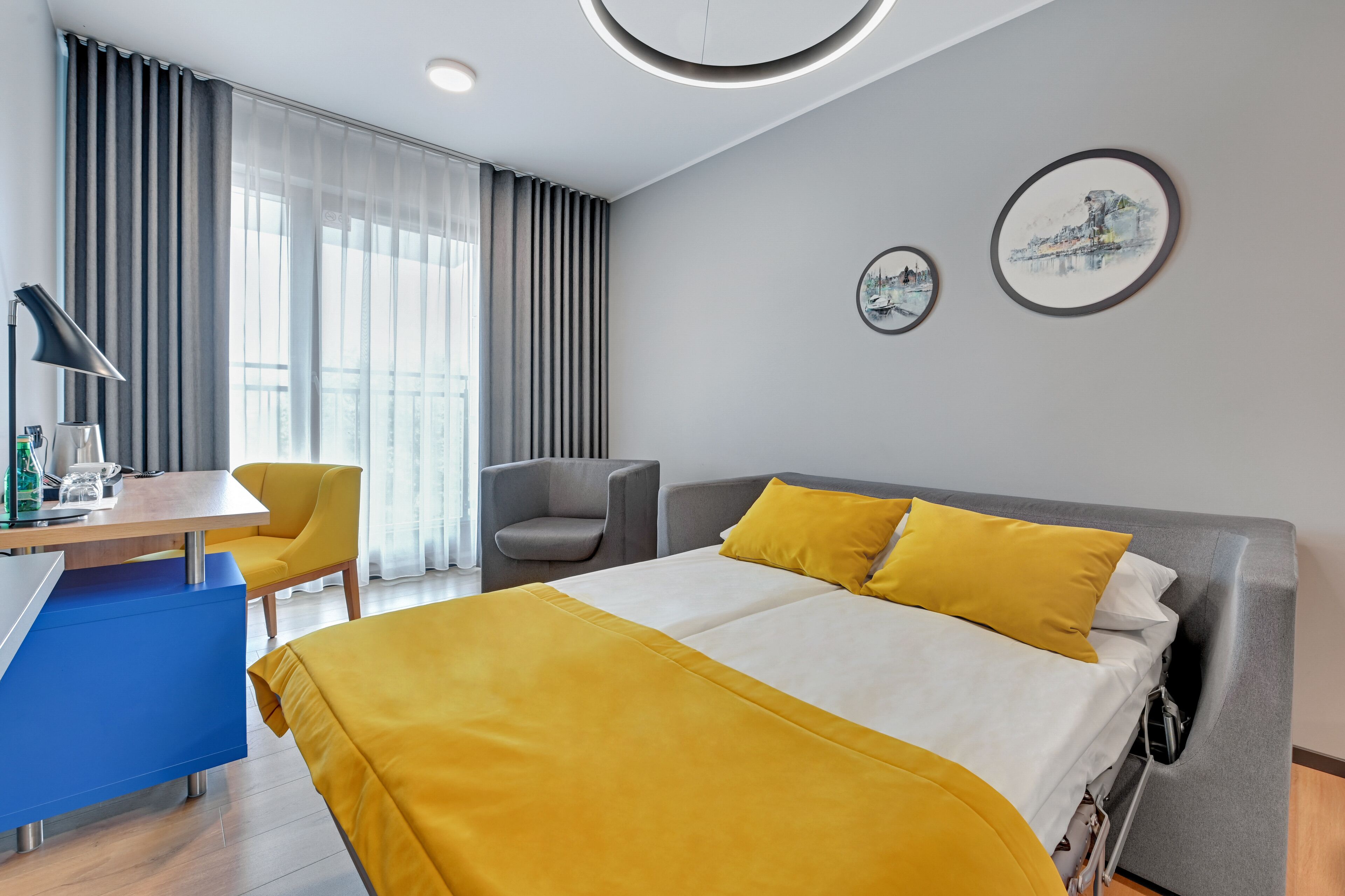 Une chambre d’hôtel avec un lit, un bureau, une chaise et une fenêtre avec des rideaux.