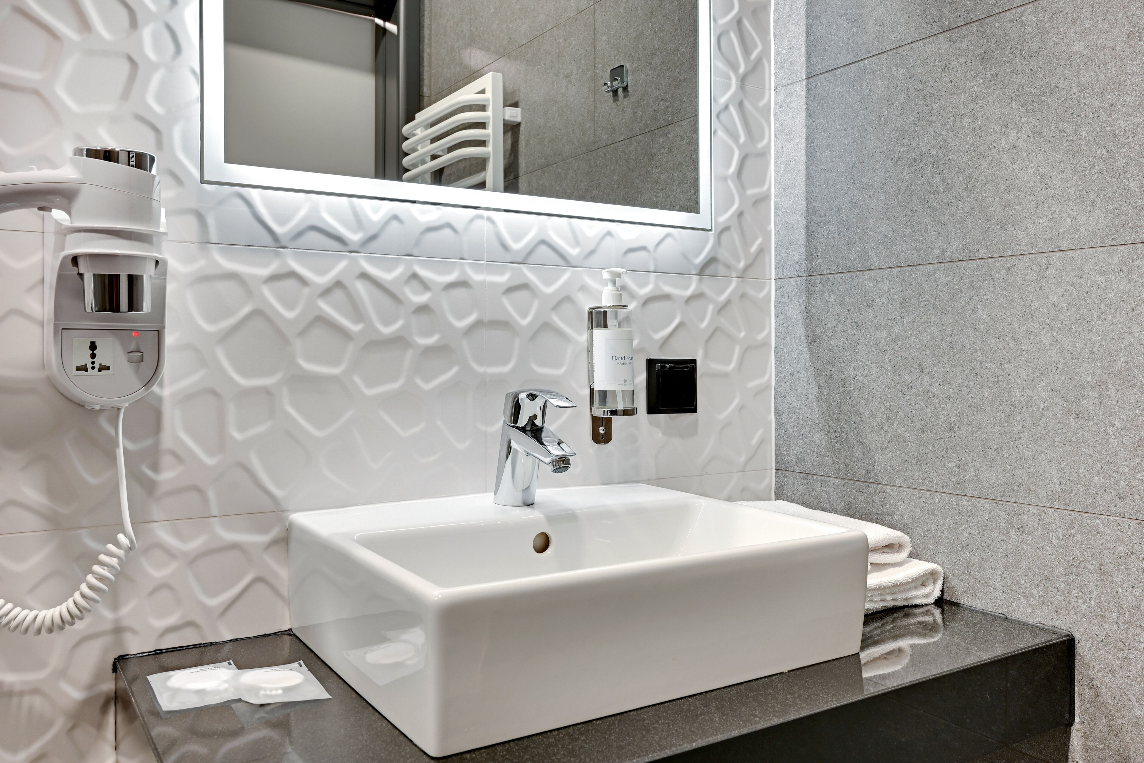 A modern bathroom with a white sink, a hand dryer, and a towel rack.