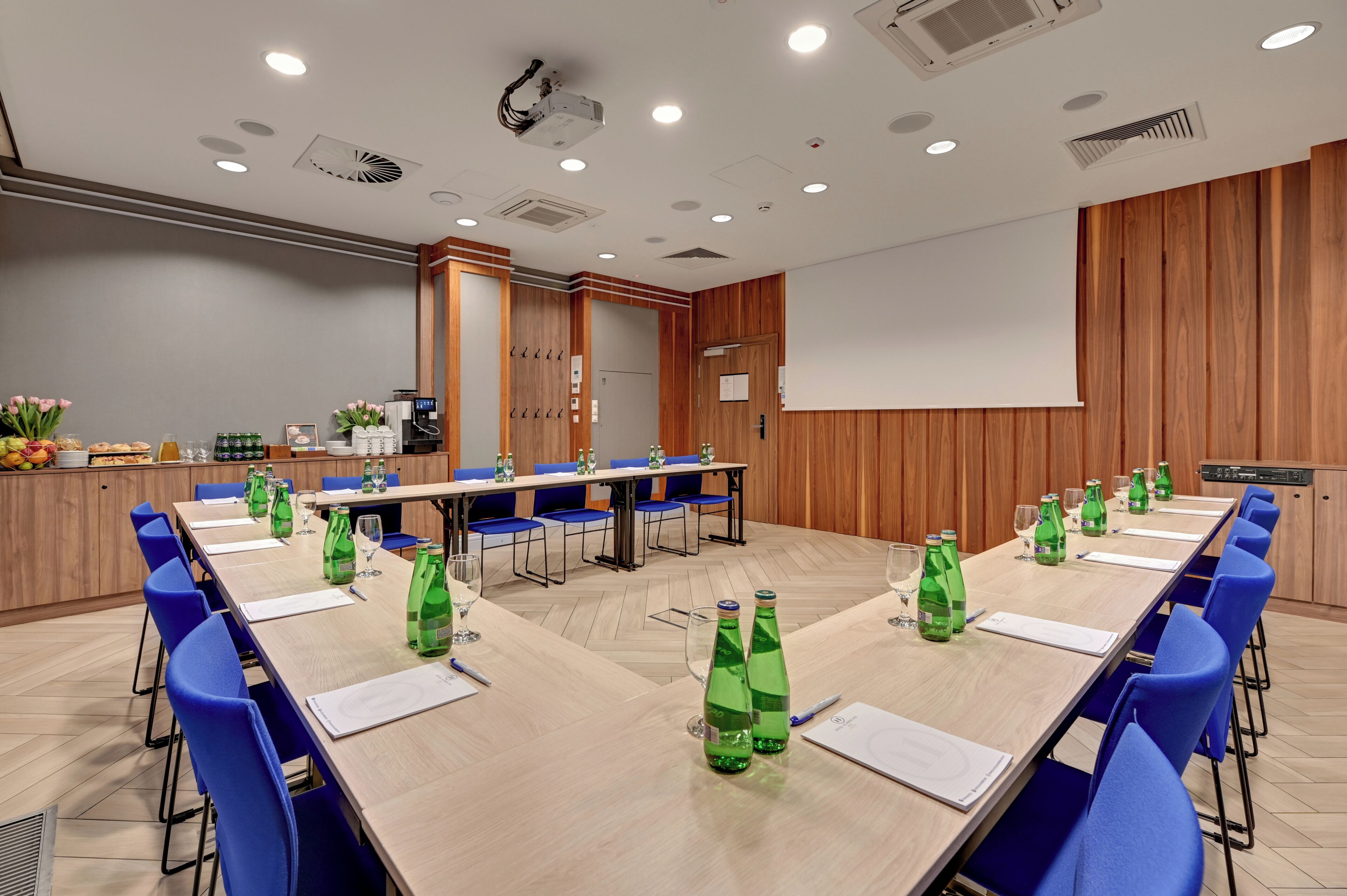 Een vergaderzaal met een lange tafel, blauwe stoelen en groene flessen.