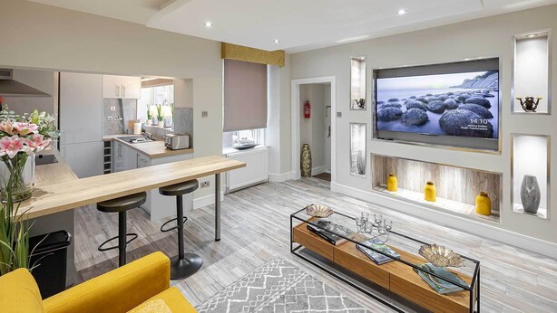 A modern kitchen with a dining area, a TV mounted on the wall, and a bar area with stools. - Carmel Apartments Queen Street Residence (Falkirk)