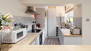 A compact kitchen with a microwave, toaster, and kettle on the counter, a sink, and a stove. - Carmel Apartments Queen Street Residence (Falkirk)