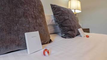 Una cama bien hecha con un almohadón blanco y una caja blanca con la etiqueta 'SLEEP WELL' a la izquierda.