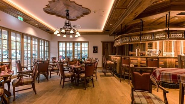 Un restaurante con mobiliario de madera, ventanas amplias y una zona de bar.