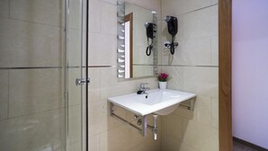 Un baño con cabina de ducha de vidrio, un lavabo blanco con espejo y un secador de pelo montado en la pared.