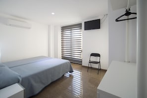 A modern hotel room with a single bed, a chair, a flat-screen TV mounted on the wall, and a window with blinds. - Drassanes (Barcelona)