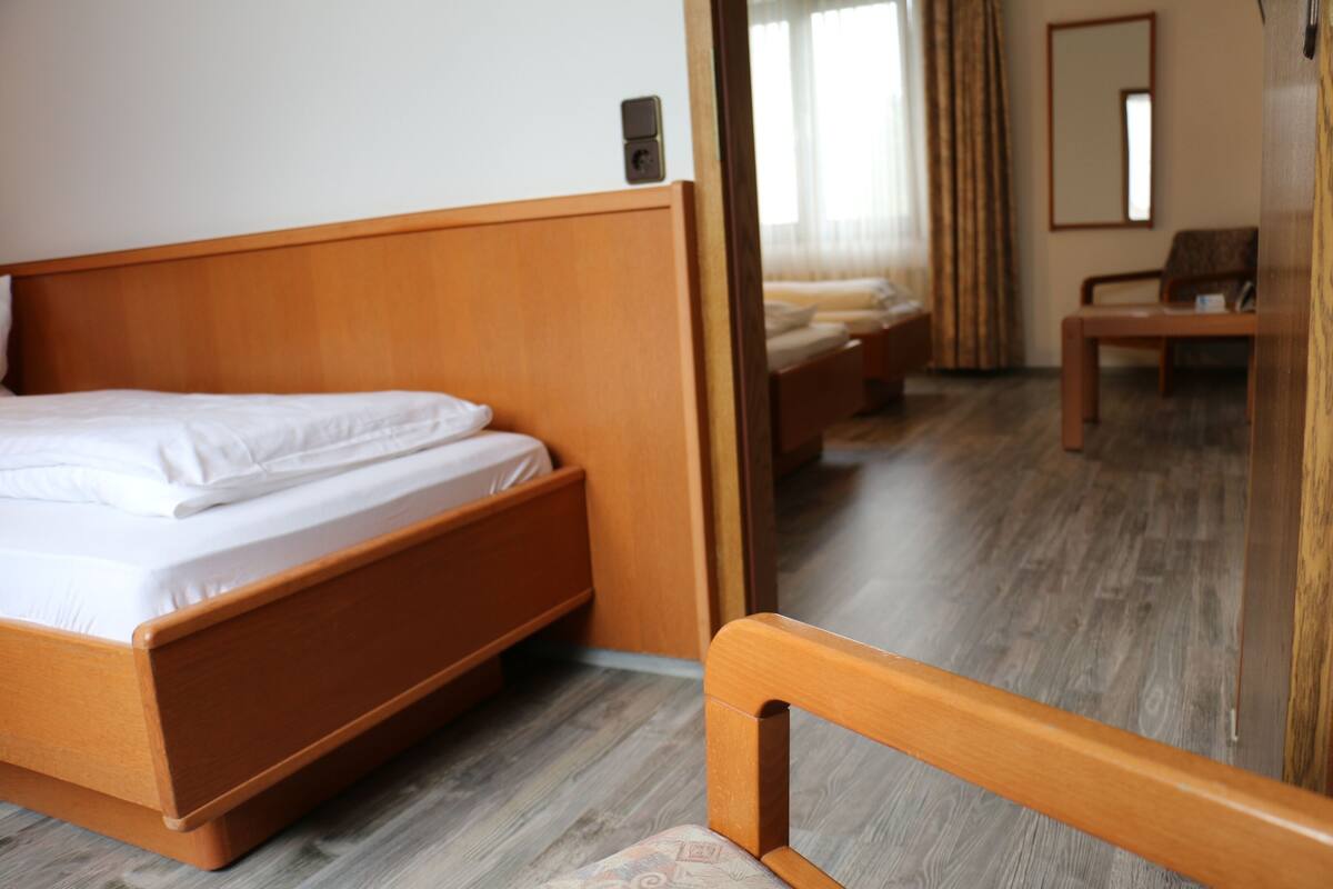 A hotel room with a wooden bed, a wooden chair, a wooden desk, and a mirror on the wall.