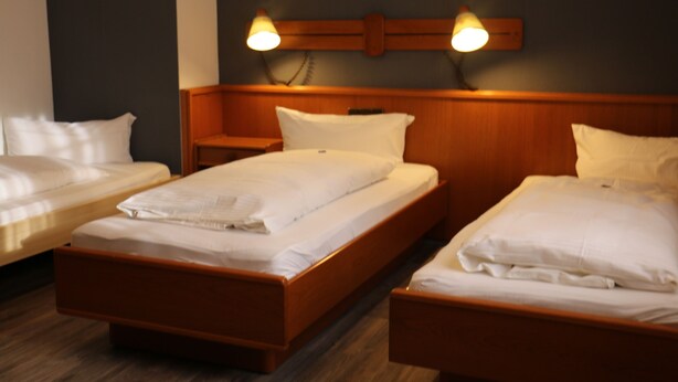 A hotel room with three single beds, wooden headboards, and bedside lamps. - Hotel Alt Steinbach (Steinbach)