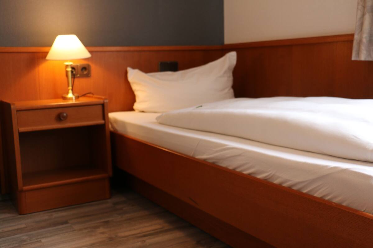 A neatly made bed with white linens, a wooden nightstand with a lamp, and a wooden headboard.