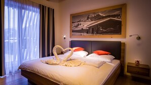 A hotel room with a large bed, a painting of a snowy mountain landscape, and a heart-shaped towel arrangement on the bed. - Apartments Dolomit Royal (Sillian)