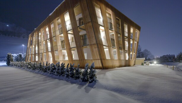 A modern building with a unique geometric facade, large windows, and a snow-covered ground. - Apartments Dolomit Royal (Sillian)