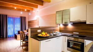 A modern kitchen with wooden beams, white cabinets, and a built-in oven. - Apartments Dolomit Royal (Sillian)