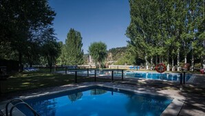 A rectangular swimming pool with a metal safety railing, surrounded by trees and a grassy area with lounge chairs. - Camping & Bungalows Ligüerre de Cinca (Abizanda)