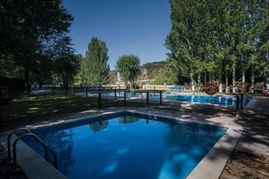 Piscina rectangular con barandilla de seguridad metálica, rodeada de árboles y un área verde con sillas de descanso.