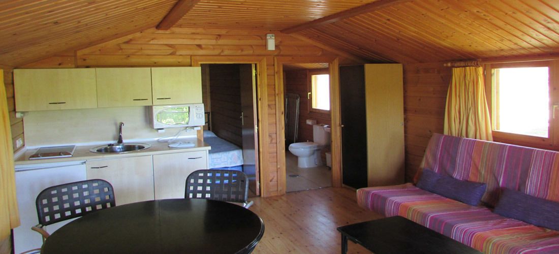 Interior de una cabaña con cocina, comedor y sofá.