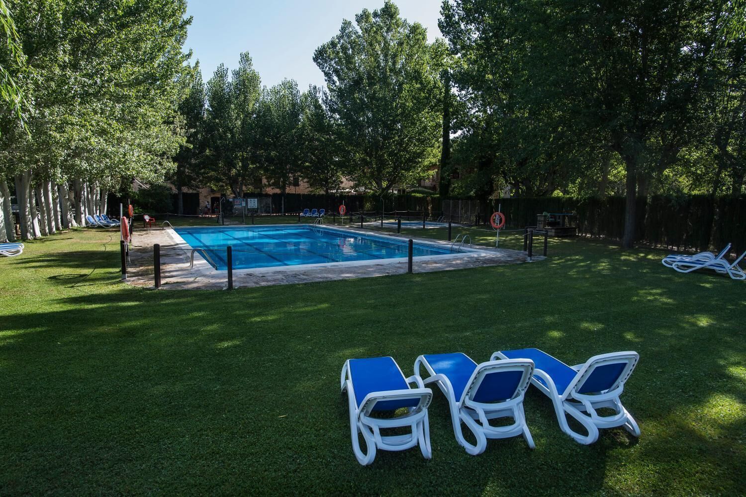 A swimming pool surrounded by grass and trees, with lounge chairs and a fence.