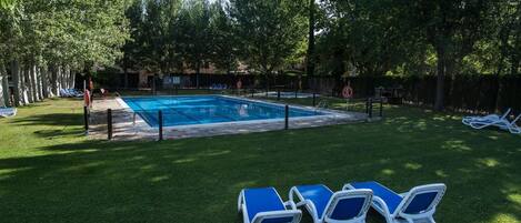 A swimming pool surrounded by grass and trees, with lounge chairs and a fence.