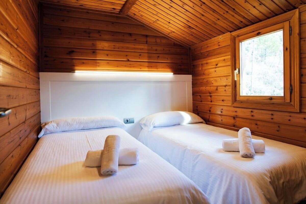A cabin-style room with two beds, wooden walls, a window, and a ceiling light.