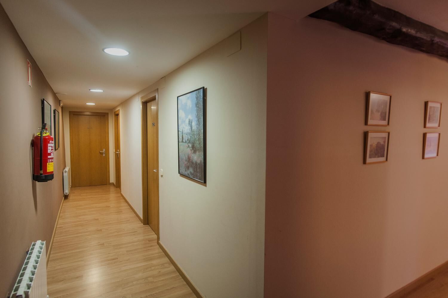 Un pasillo con piso de madera, un extintor y cuadros en las paredes.