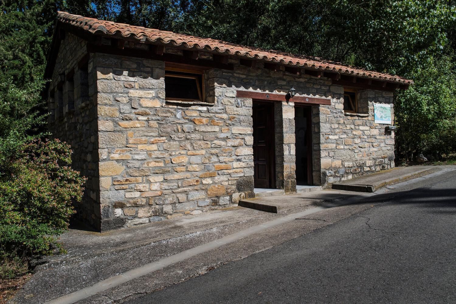 Un edificio de piedra con tejado de tejas, dos puertas de madera y un pequeño porche.