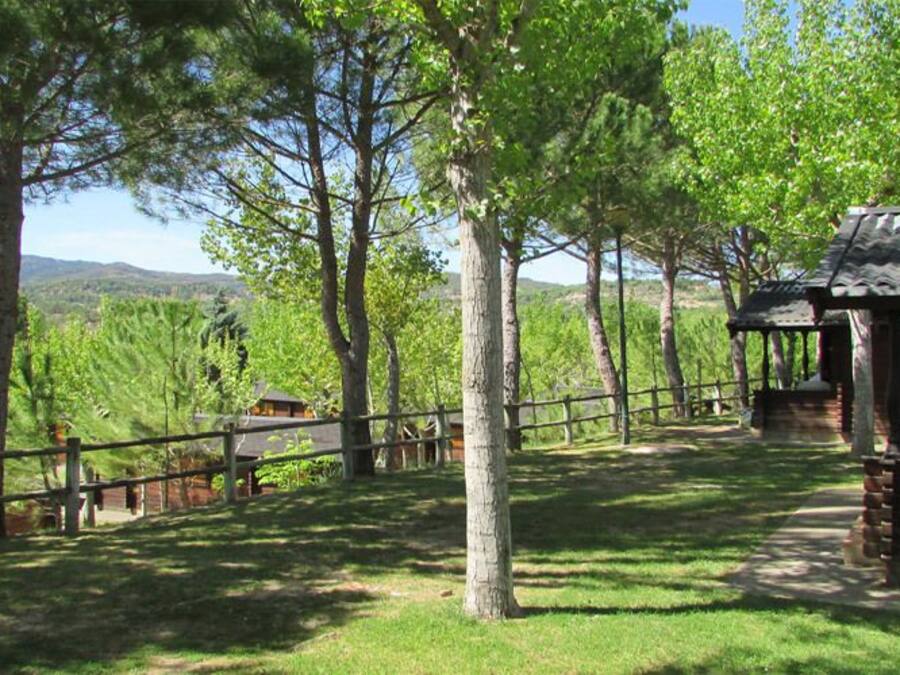 Una cabaña rústica con fachada de madera, rodeada por un patio cercado con árboles y una vista despejada del paisaje.