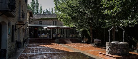 A courtyard with a stone fountain, outdoor seating area, and a building with a tiled roof.
