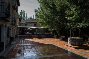 Un patio con una fuente de piedra, zona de estar al aire libre y un edificio con tejado de azulejos.