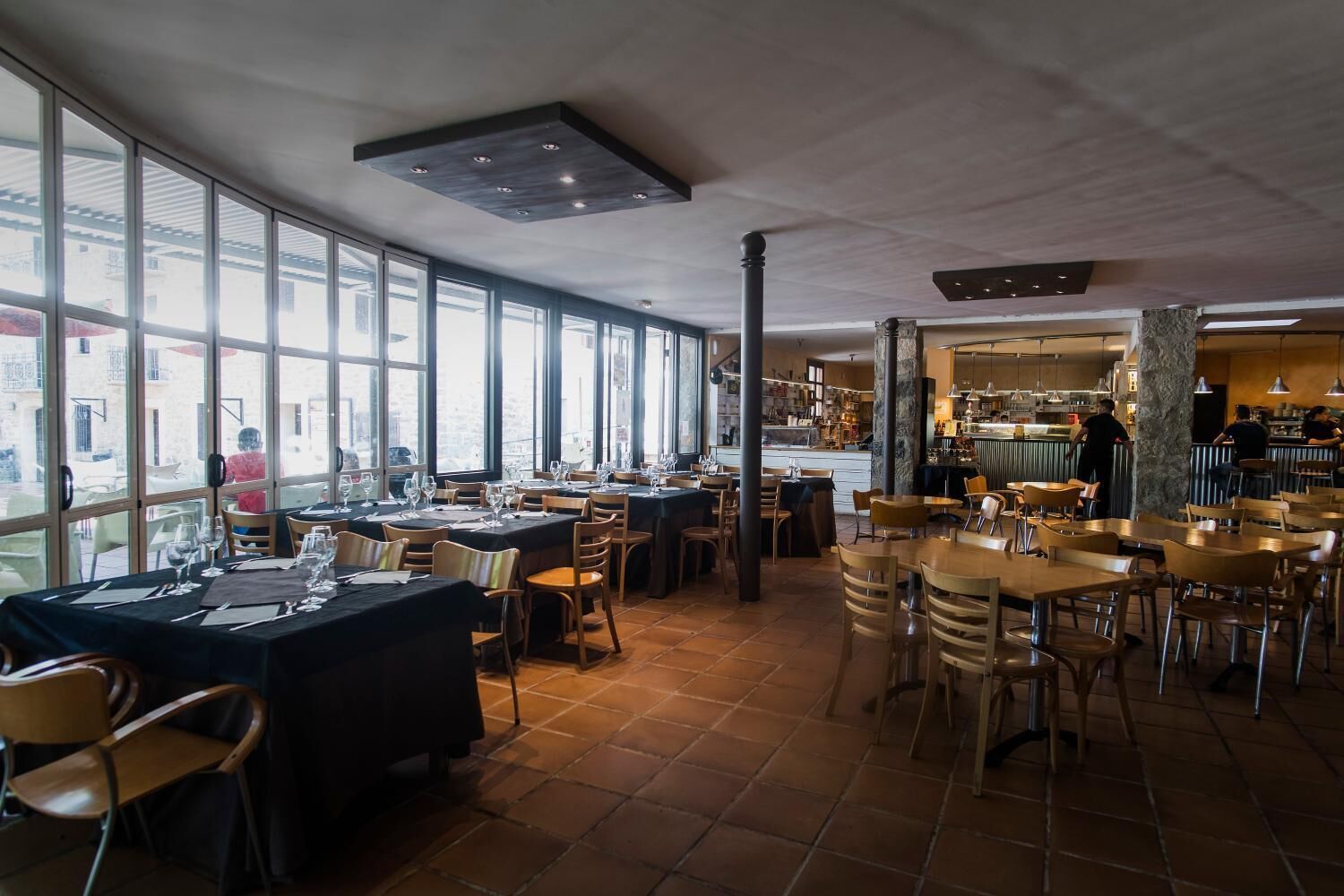 A restaurant with large windows, tiled floor, and multiple dining tables and chairs.