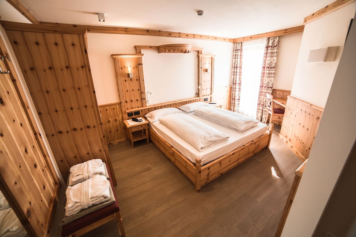 A wooden-paneled room with a large bed, a bedside table, a chair, and a wardrobe.