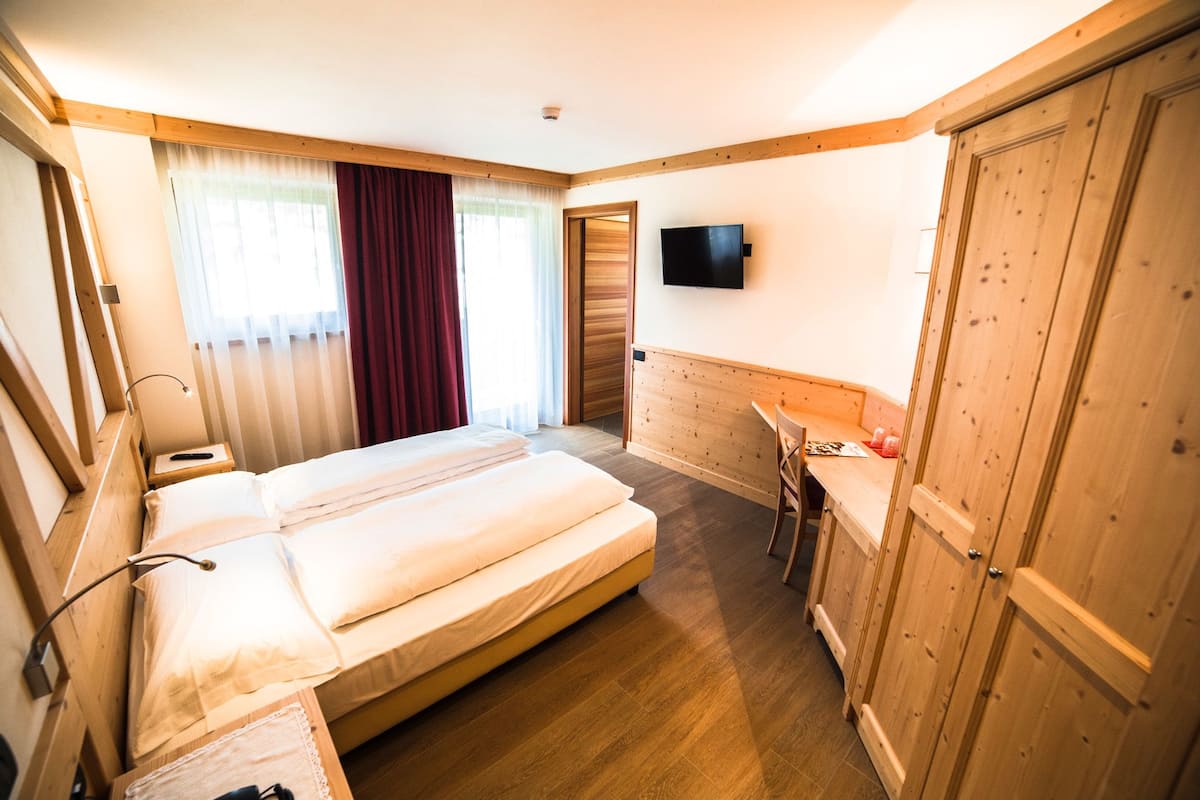 A hotel room with a bed, a desk, a TV, and wooden furniture.