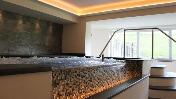 Un área de spa con un jacuzzi con mosaicos, una pared de piedra y una ventana con vista a la vegetación.