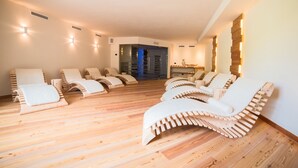 Un cuarto de spa con suelo de madera, varios camastros y una zona de sauna visible al fondo.