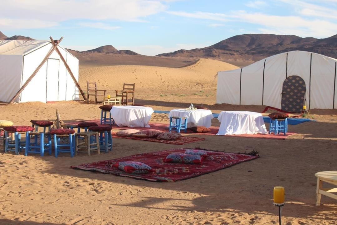 A desert campsite with tents, tables, chairs, and rugs.