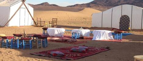 A desert campsite with tents, tables, chairs, and rugs.