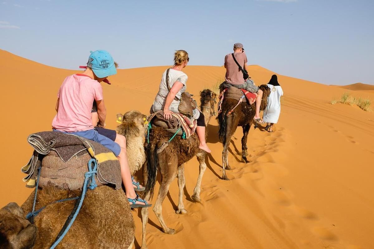 Um grupo de pessoas cavalgando camelos por uma paisagem desértica.