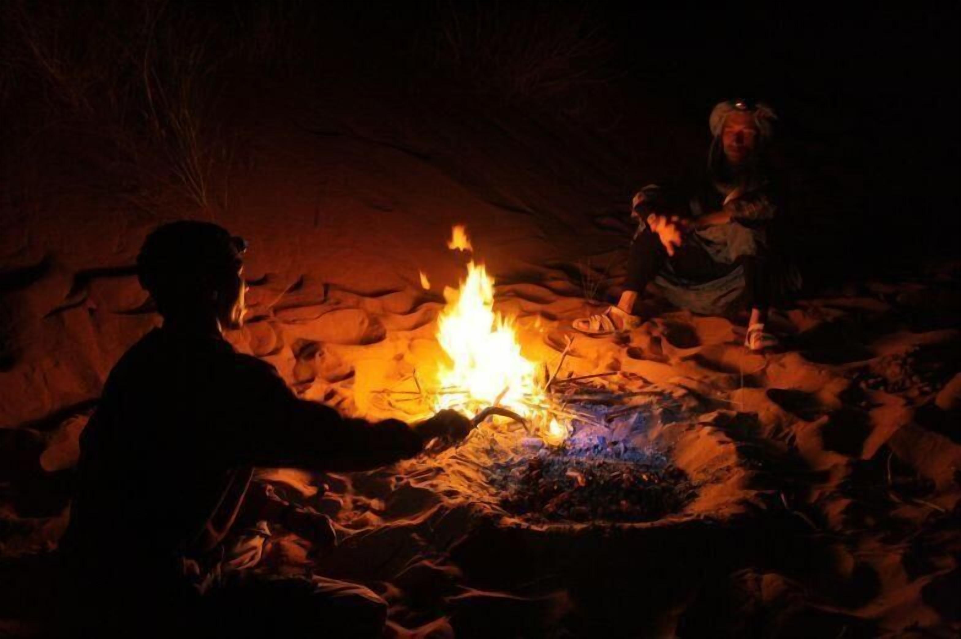 Uma fogueira com pessoas sentadas ao redor em um ambiente natural rochoso.