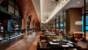 Un restaurante espacioso con arcos de ladrillo, lámparas modernas y una larga barra.