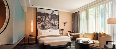 A modern hotel room with a large bed, a sofa, a round coffee table, and a cityscape painting on the wall.