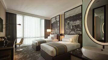 A hotel room with two beds, a desk with a chair, a large mirror, and a round sink.