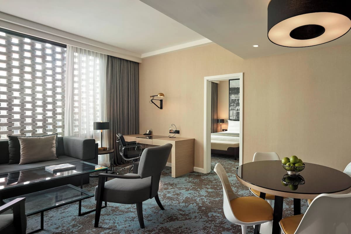 Ein Hotelzimmer mit Wohnbereich, einem Esstisch mit Obst, einem Schreibtisch und einem Bett.