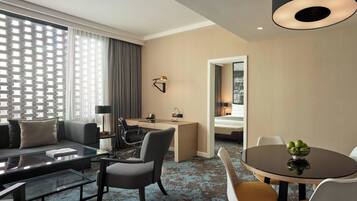 Habitación de hotel con sala de estar, una mesa de comedor con fruta, un escritorio y una cama.