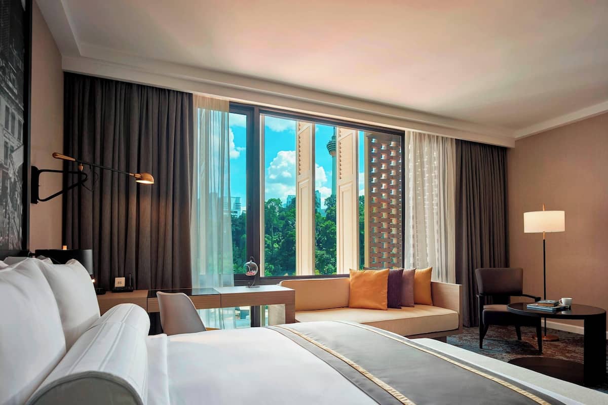 Ein Hotelzimmer mit großem Fenster, einem Bett, einem Schreibtisch, einem Stuhl und einer Couch.
