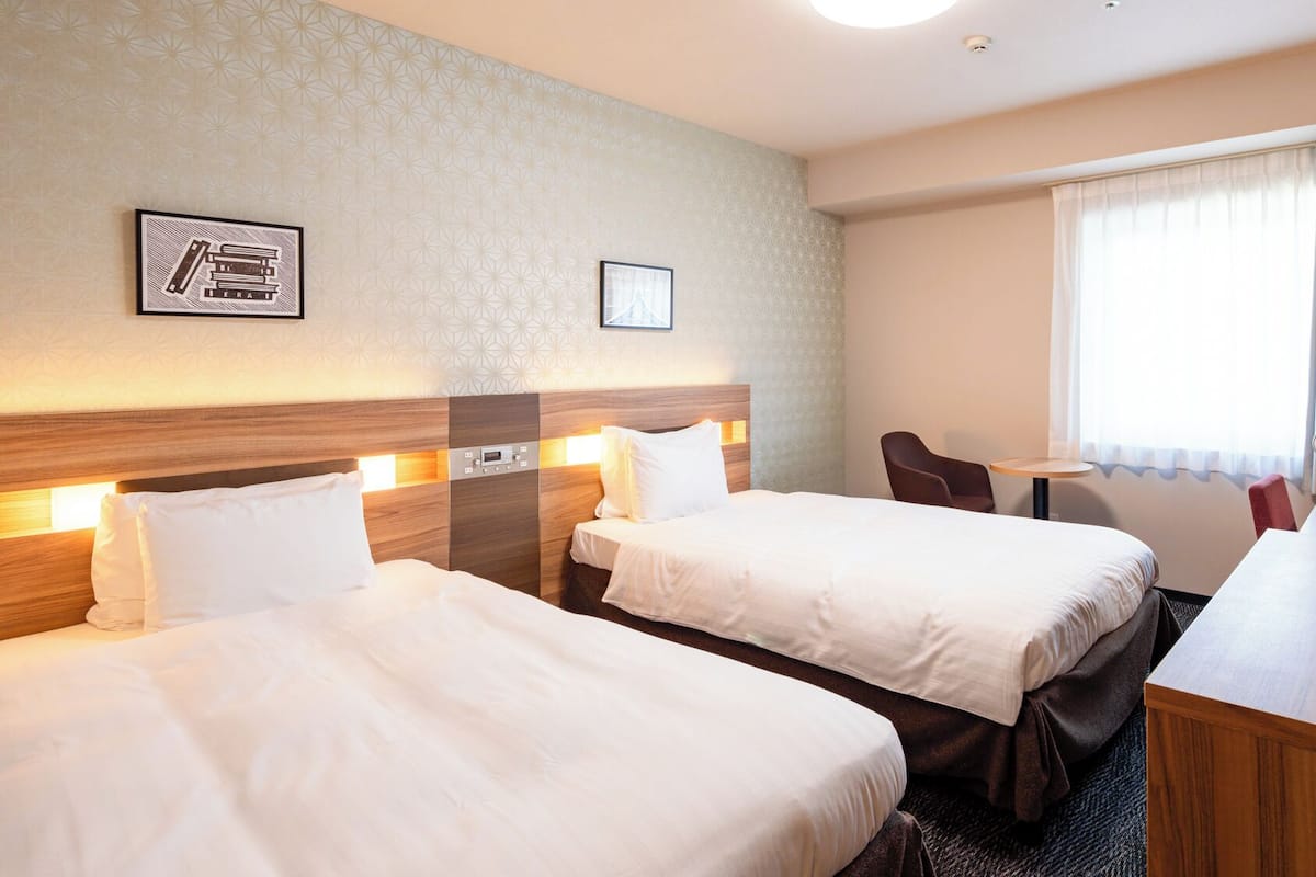 A hotel room with two beds, a desk, a chair, a small table, and a wardrobe.